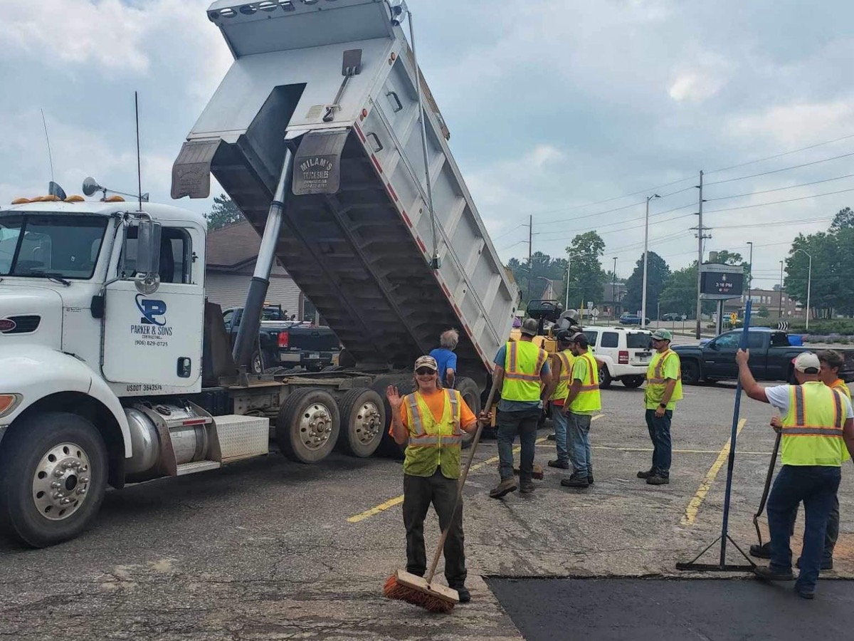 Parker and Sons dump truck with its box raised on a parking lot paving job, crew working alongside