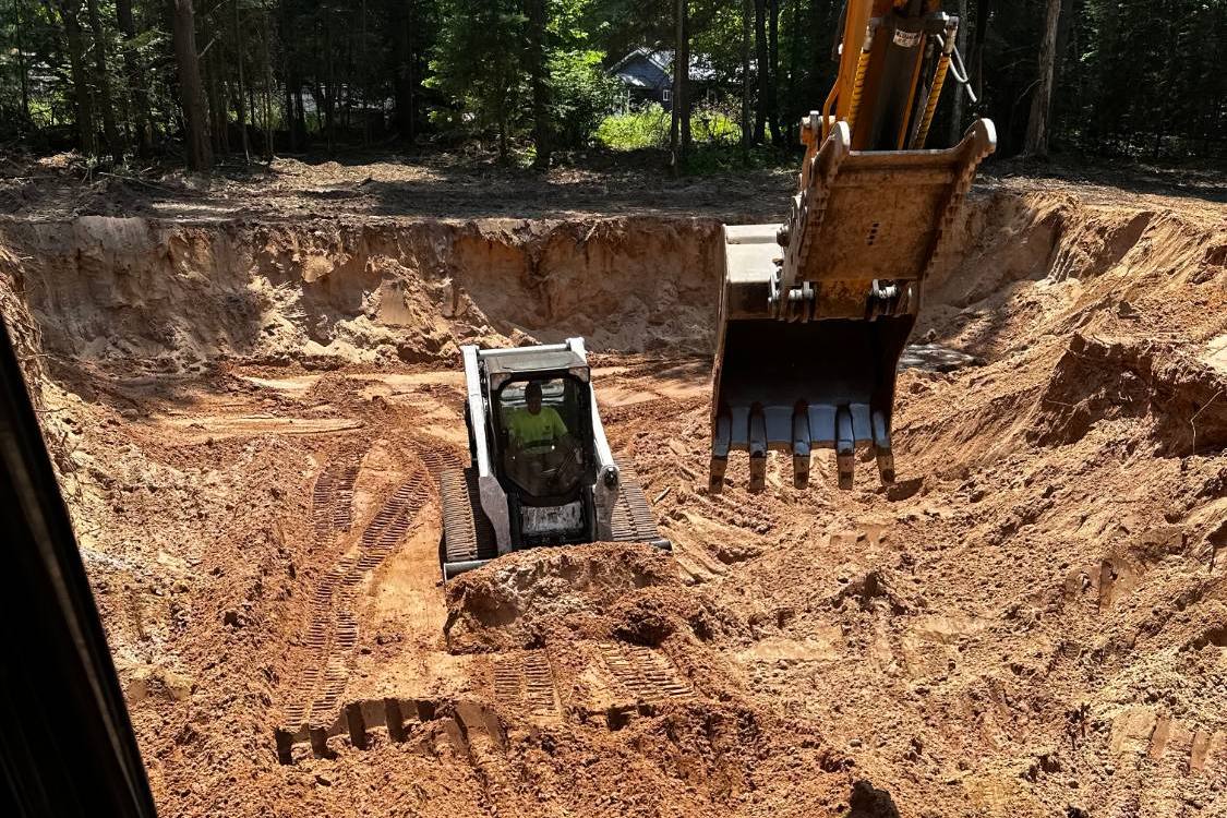 View from the excavator cab into a basement excavation, a skid steer working the bottom