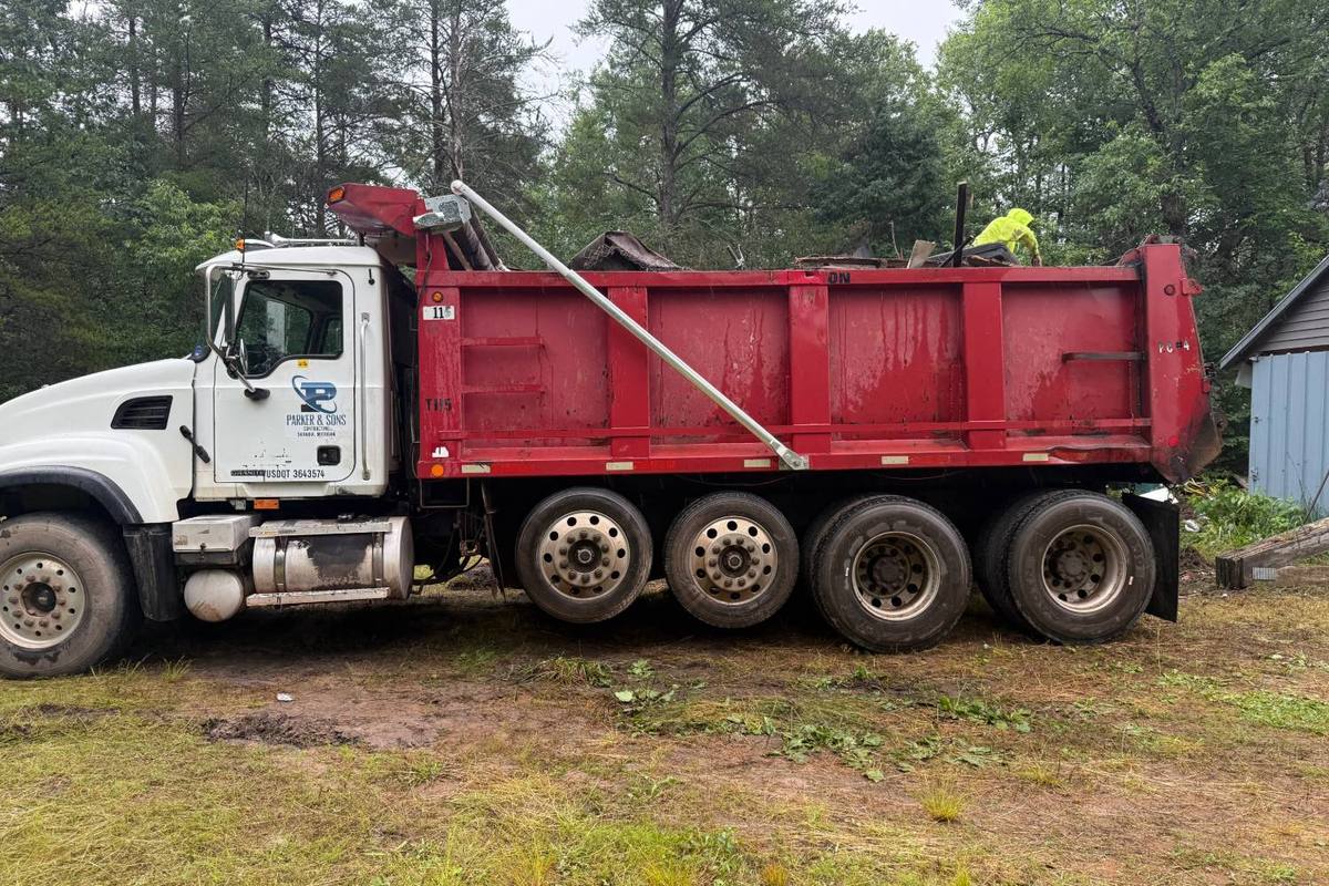 Parker and Sons dump truck loaded with demolition debris, a worker leveling the load on top