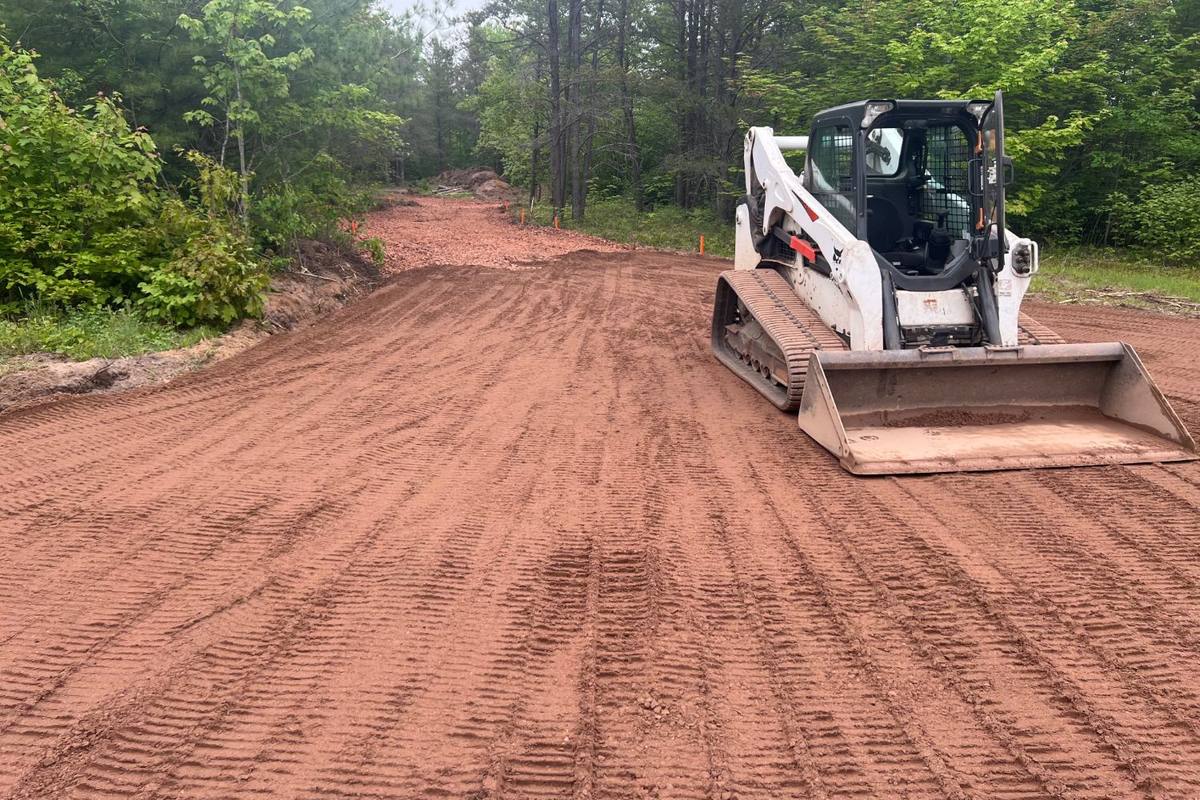 Track loader finishing a new graded road through the woods, with the edges staked