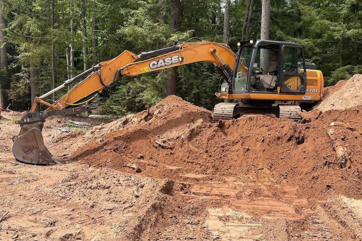 Parker and Sons Case excavator parked on a pile of red soil at a wooded job site