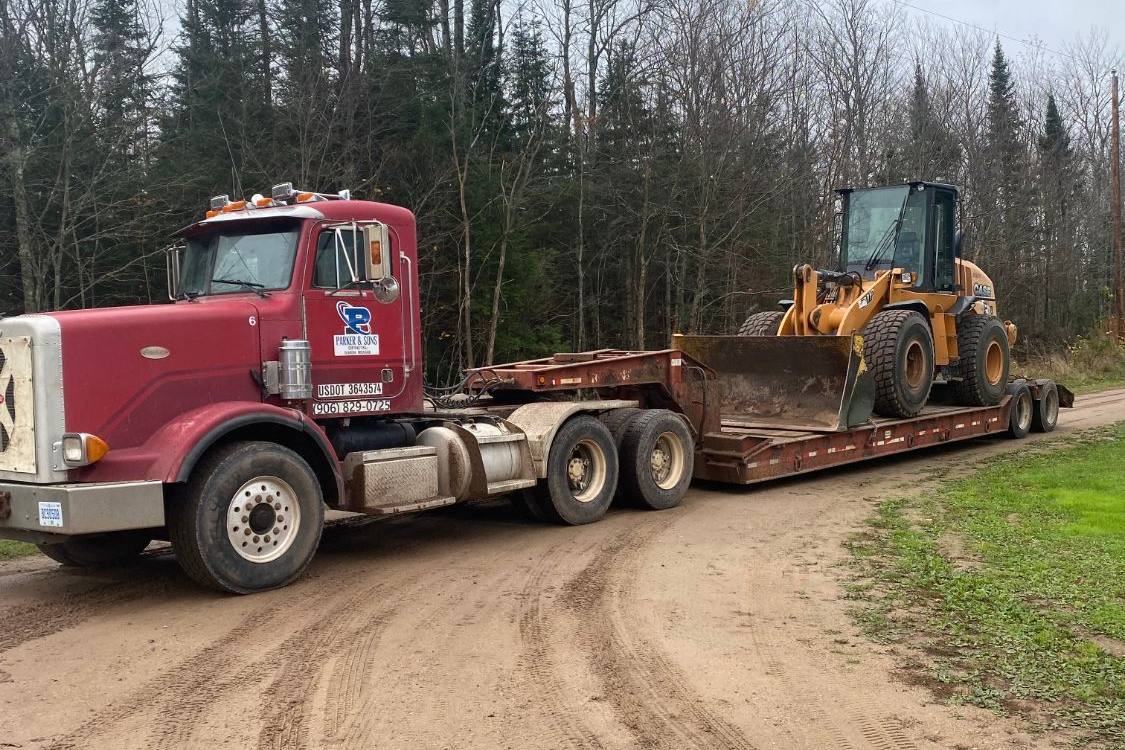 Case wheel loader on a lowboy trailer behind a maroon Parker and Sons Peterbilt