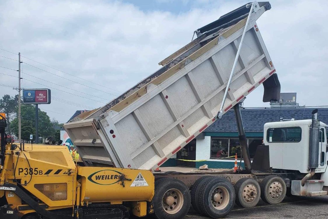 Dump truck raising its box to feed asphalt into a paving machine in a parking lot
