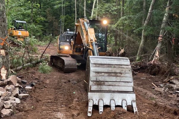 Excavator cutting a new road through the woods, with a second machine working behind it