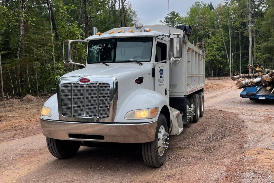 White Parker and Sons Peterbilt dump truck on a gravel site road in the woods