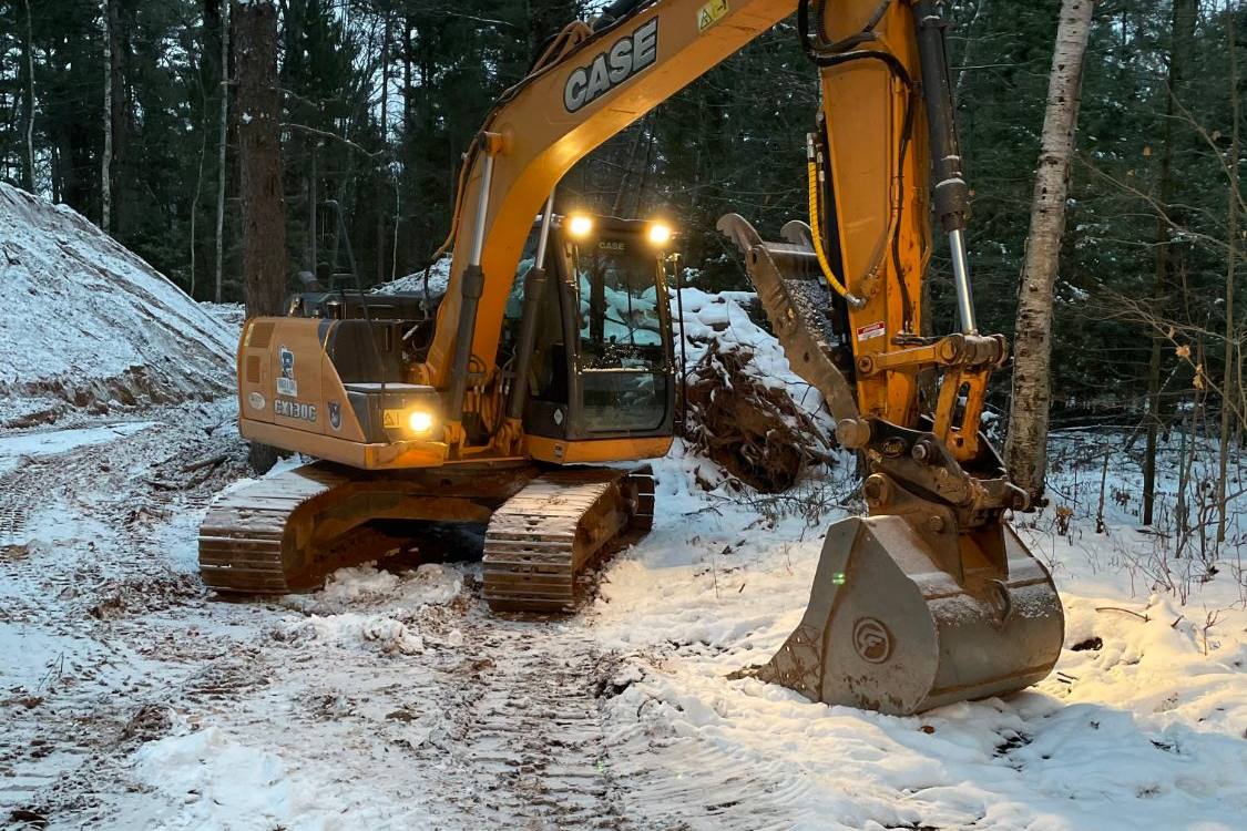 Case excavator with its work lights on at a snowy wooded job site